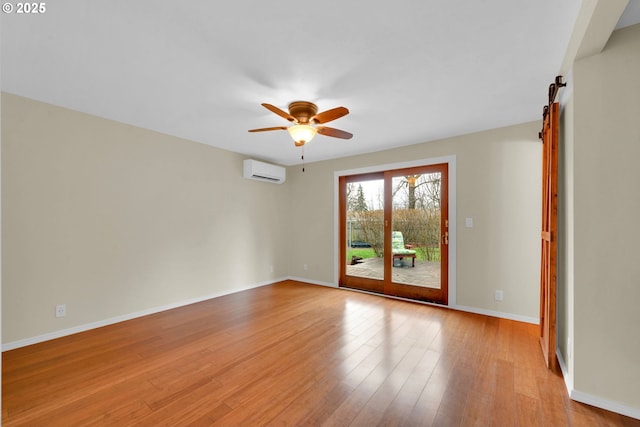 spare room featuring ceiling fan, light hardwood / wood-style flooring, a barn door, and a wall mounted AC