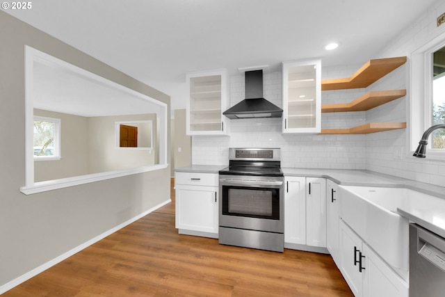 kitchen featuring wall chimney range hood, sink, white cabinetry, stainless steel appliances, and light wood-type flooring