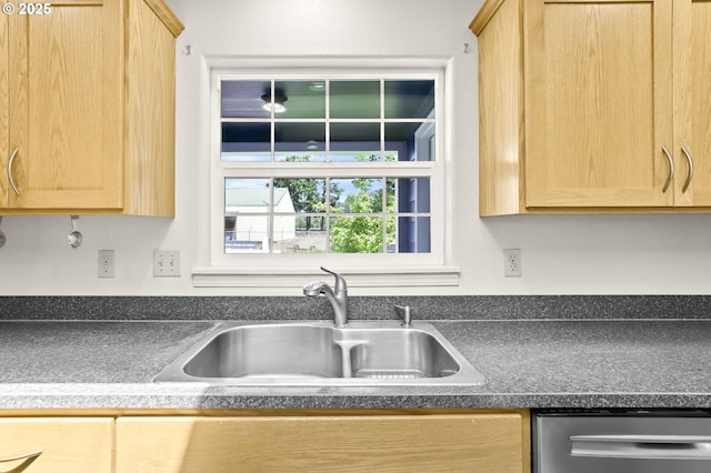 kitchen featuring a sink, stainless steel dishwasher, light brown cabinetry, and dark countertops