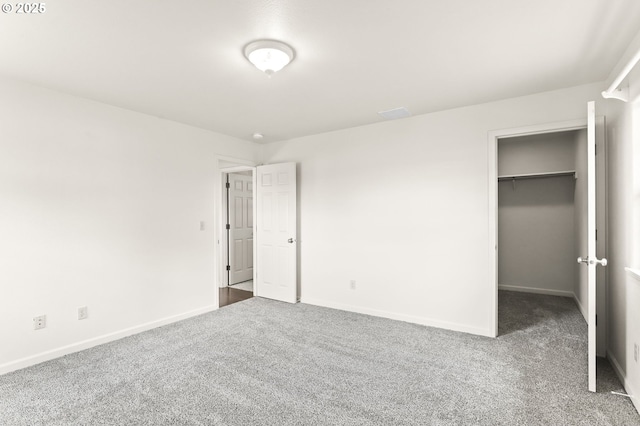 unfurnished bedroom with carpet floors, a spacious closet, baseboards, and a closet