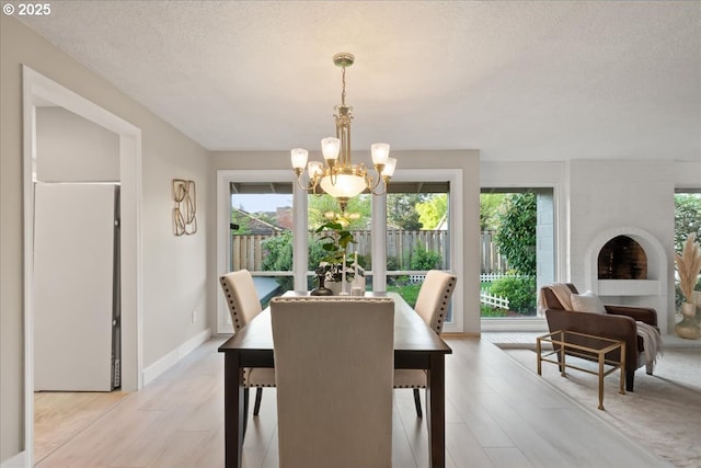 dining area featuring a textured ceiling, a notable chandelier, baseboards, and light wood-type flooring