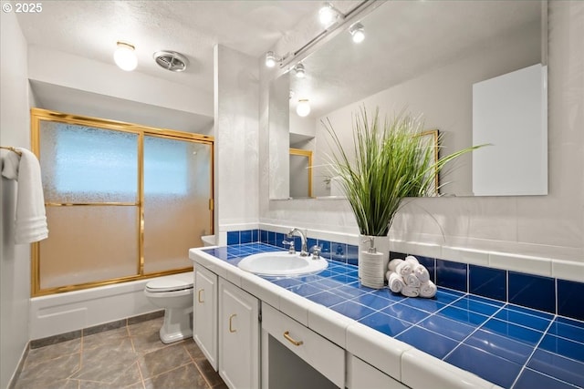 bathroom with vanity, toilet, baseboards, combined bath / shower with glass door, and visible vents
