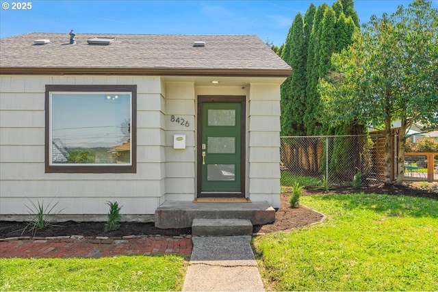 doorway to property with roof with shingles, fence, and a yard