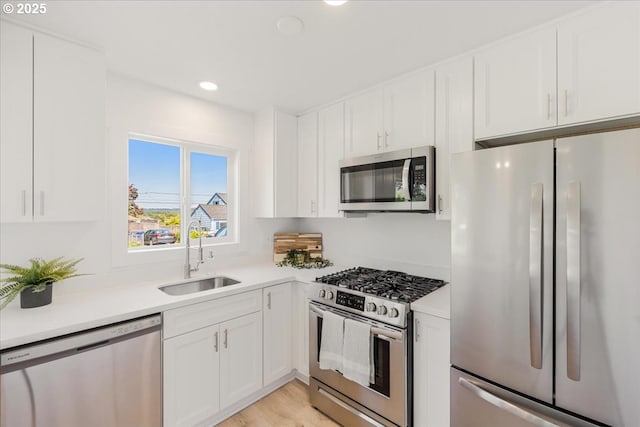 kitchen featuring appliances with stainless steel finishes, a sink, light countertops, white cabinets, and recessed lighting