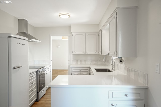 kitchen featuring a peninsula, a sink, light countertops, freestanding refrigerator, and stainless steel electric range oven