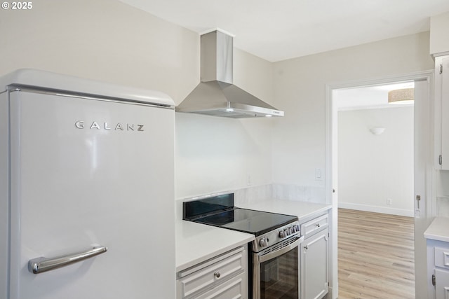 kitchen with refrigerator, light wood-style floors, light countertops, stainless steel electric stove, and wall chimney exhaust hood