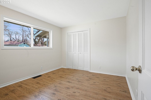 unfurnished bedroom with a closet, visible vents, baseboards, and wood finished floors