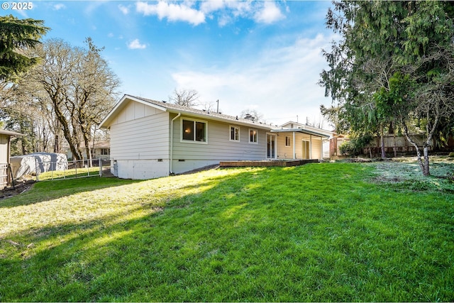 rear view of property with board and batten siding, crawl space, fence, and a lawn