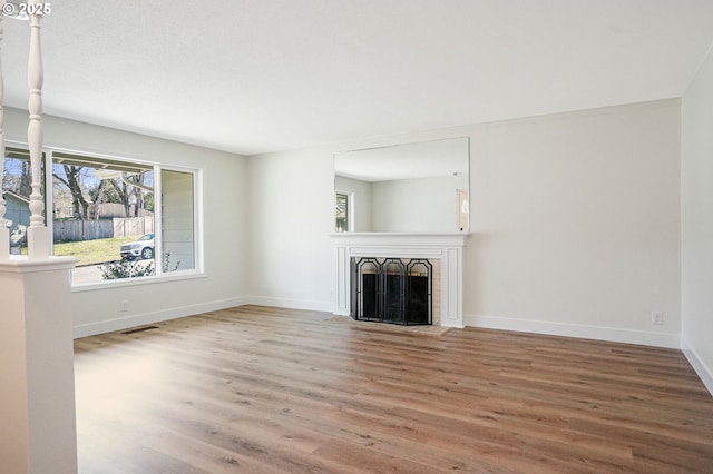 unfurnished living room featuring baseboards, a fireplace with flush hearth, visible vents, and wood finished floors