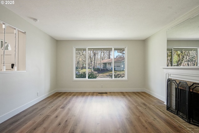 unfurnished living room with wood finished floors, plenty of natural light, a fireplace with flush hearth, and visible vents