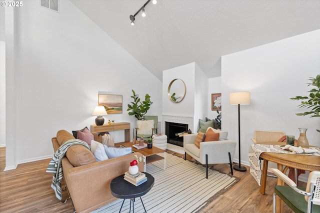 living room with a brick fireplace, light hardwood / wood-style flooring, rail lighting, and vaulted ceiling