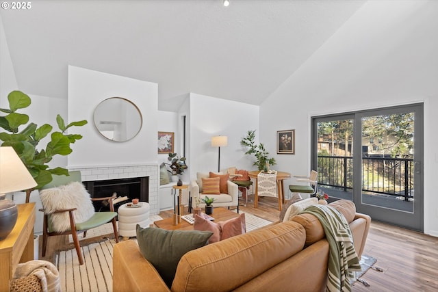 living room with a fireplace, high vaulted ceiling, and light hardwood / wood-style flooring