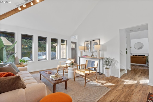 living room with beamed ceiling, rail lighting, light hardwood / wood-style floors, and high vaulted ceiling