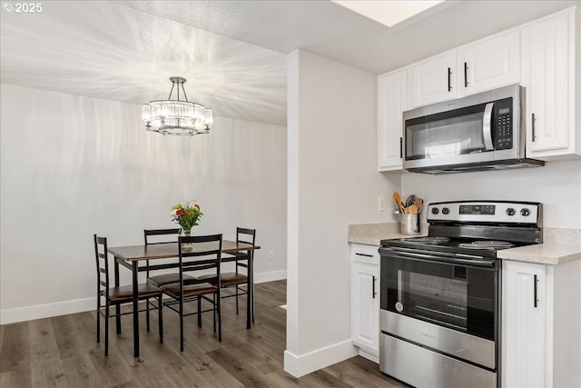 kitchen with appliances with stainless steel finishes, dark wood-type flooring, pendant lighting, an inviting chandelier, and white cabinets