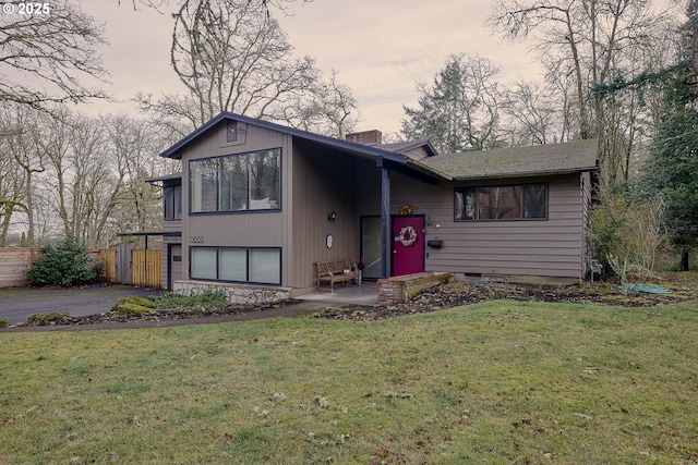 view of front of property featuring a patio, aphalt driveway, fence, a lawn, and a chimney