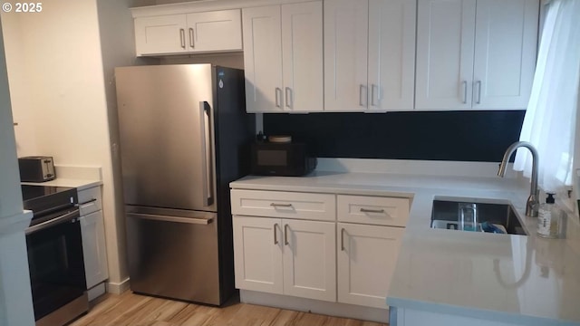 kitchen with light countertops, range with electric stovetop, freestanding refrigerator, white cabinetry, and a sink