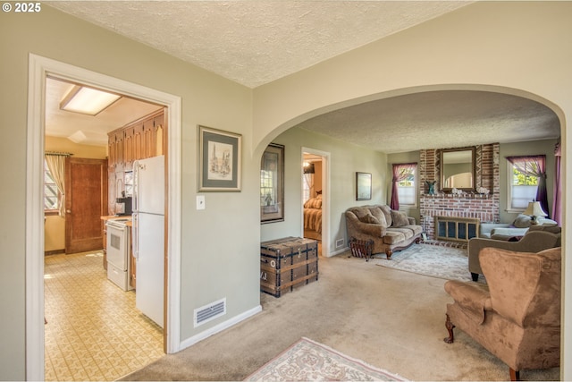 living room featuring arched walkways, a textured ceiling, light colored carpet, baseboards, and a brick fireplace