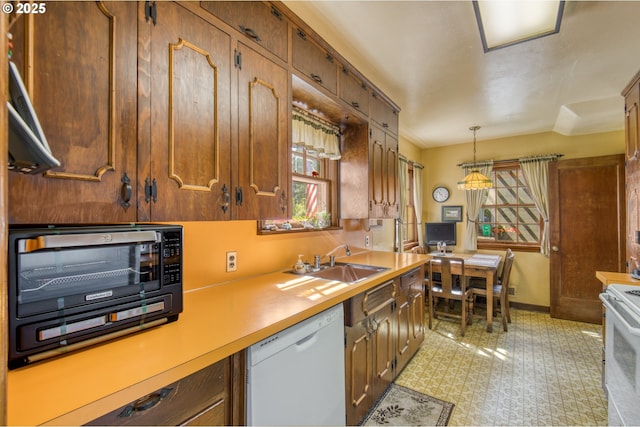 kitchen with white appliances, a sink, light countertops, pendant lighting, and baseboards