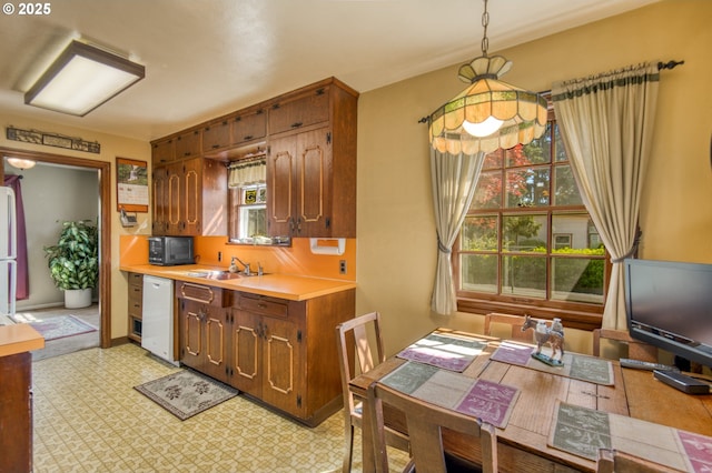 kitchen featuring dishwasher, light countertops, a sink, hanging light fixtures, and light floors
