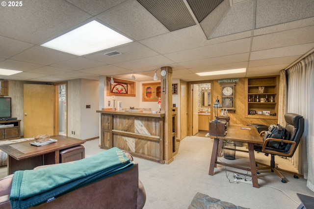 living area with light colored carpet, a drop ceiling, bar area, wooden walls, and built in features