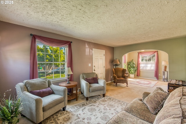 living area featuring arched walkways, carpet floors, healthy amount of natural light, a textured ceiling, and baseboards