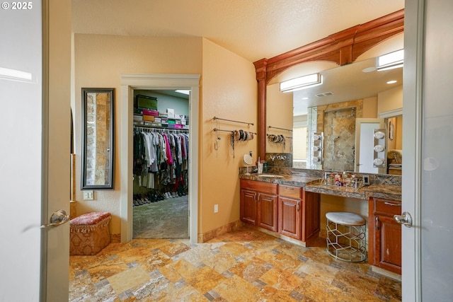 bathroom with stone finish flooring, vanity, a textured ceiling, tiled shower, and baseboards