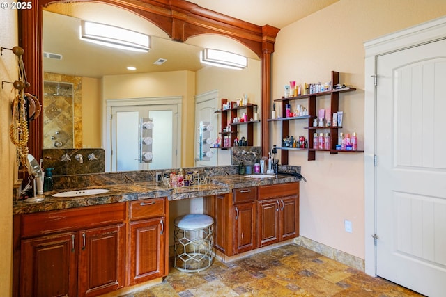 full bath with stone finish floor, visible vents, a sink, and double vanity