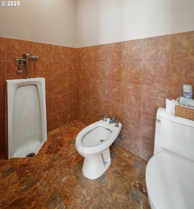 bathroom featuring toilet, a bidet, and tile walls