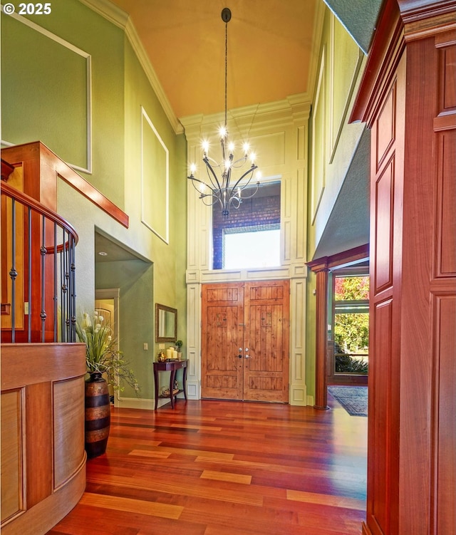 foyer entrance featuring a notable chandelier, wood finished floors, a towering ceiling, and crown molding