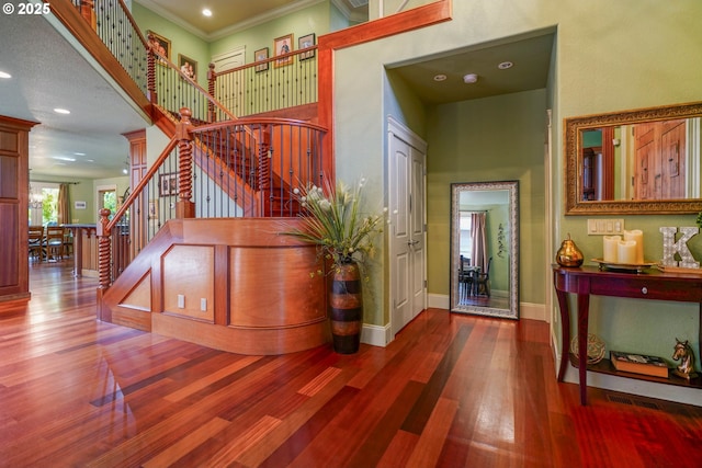 foyer with a high ceiling, wood finished floors, baseboards, stairs, and crown molding