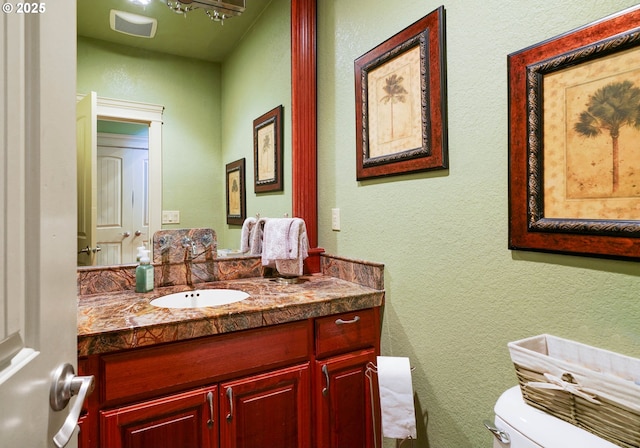 bathroom featuring visible vents, a textured wall, vanity, and toilet