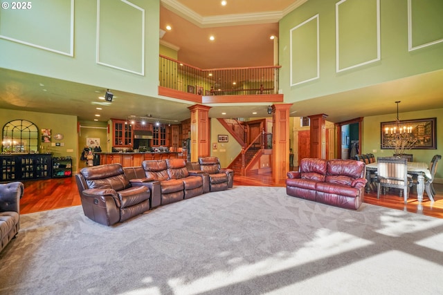 living room featuring stairway, wood finished floors, an inviting chandelier, crown molding, and ornate columns