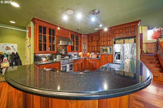 kitchen with stainless steel appliances, ventilation hood, tasteful backsplash, dark countertops, and glass insert cabinets