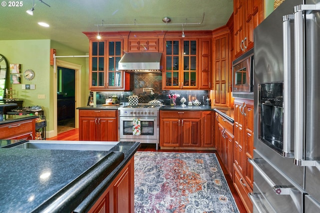 kitchen featuring tasteful backsplash, dark countertops, high quality appliances, glass insert cabinets, and extractor fan