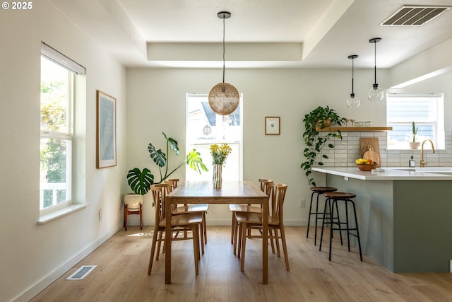 dining space featuring baseboards, a tray ceiling, light wood-type flooring, and visible vents