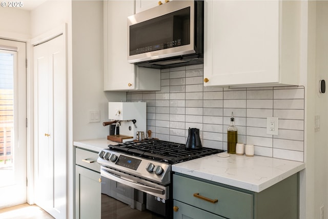 kitchen with light stone counters, decorative backsplash, stainless steel appliances, and white cabinets