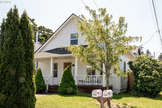 bungalow-style house with a shingled roof, a front lawn, board and batten siding, and covered porch