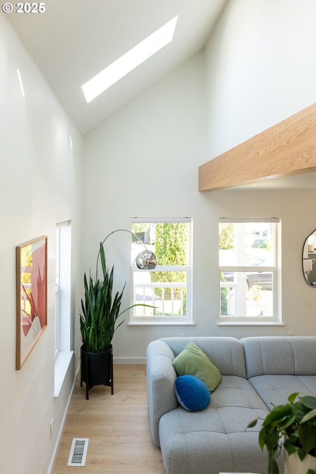 living room with visible vents, a skylight, light wood-type flooring, high vaulted ceiling, and baseboards