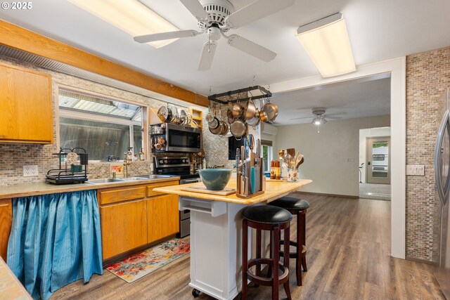 12791 Sutherland Rd, Swisshome, OR 97480 - kitchen with stainless steel appliances, a ceiling fan, wood finished floors, healthy amount of natural light, and brick wall