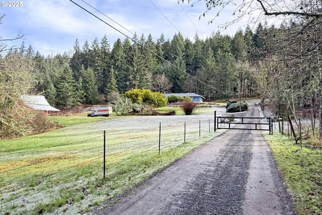 view of street with a gated entry, a gate, a view of trees, and driveway