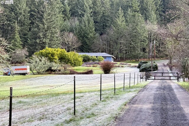 view of street featuring a gate, driveway, and a wooded view