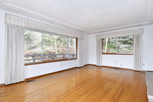 empty room with baseboards, a textured ceiling, wood finished floors, and visible vents