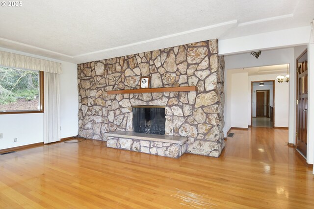 unfurnished living room with a stone fireplace, visible vents, wood finished floors, baseboards, and a notable chandelier