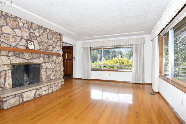 unfurnished living room with baseboards, a textured ceiling, wood finished floors, and a wealth of natural light