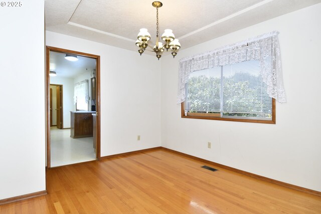 empty room featuring baseboards, visible vents, an inviting chandelier, and light wood-type flooring