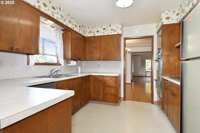 kitchen featuring a sink, brown cabinets, freestanding refrigerator, and light countertops