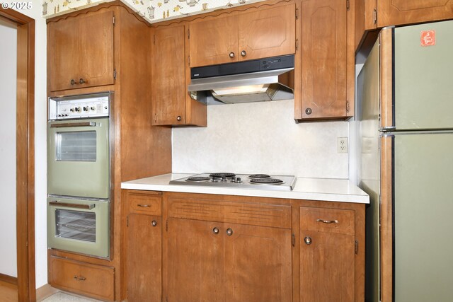 kitchen with freestanding refrigerator, double wall oven, under cabinet range hood, and light countertops