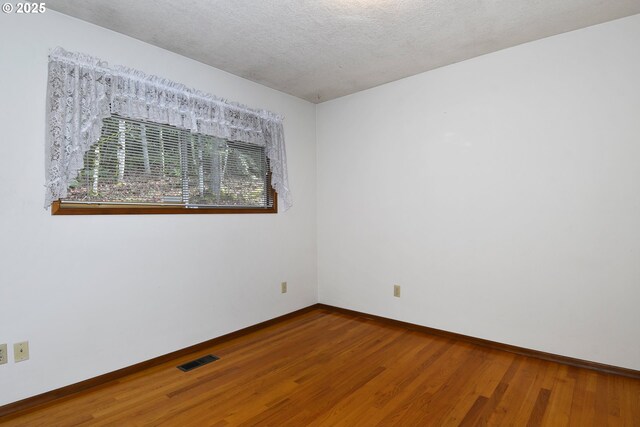 empty room featuring baseboards, a textured ceiling, wood finished floors, and visible vents
