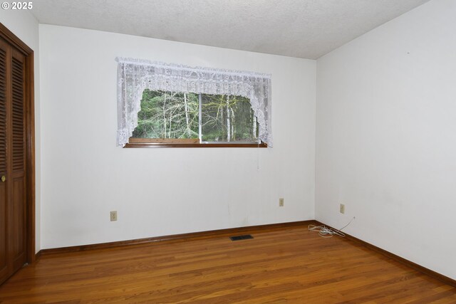 unfurnished bedroom with a textured ceiling, baseboards, wood finished floors, visible vents, and a closet