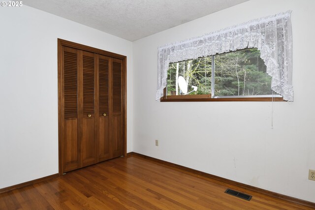 unfurnished bedroom with a textured ceiling, baseboards, wood finished floors, visible vents, and a closet
